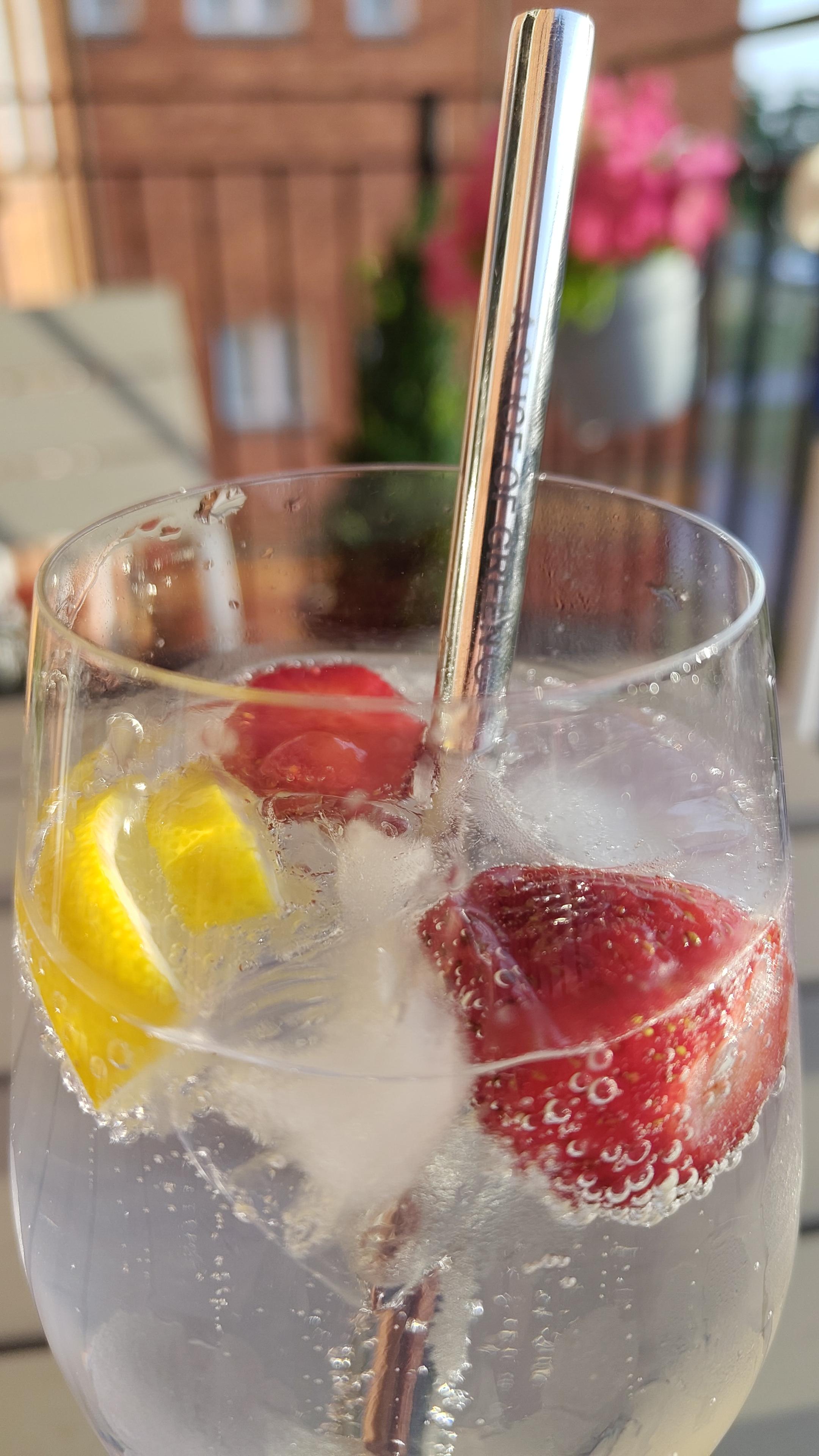 Glas med bubblande dryck, jordgubbar, citron och is. Glaset står på ett bord på en balkong.